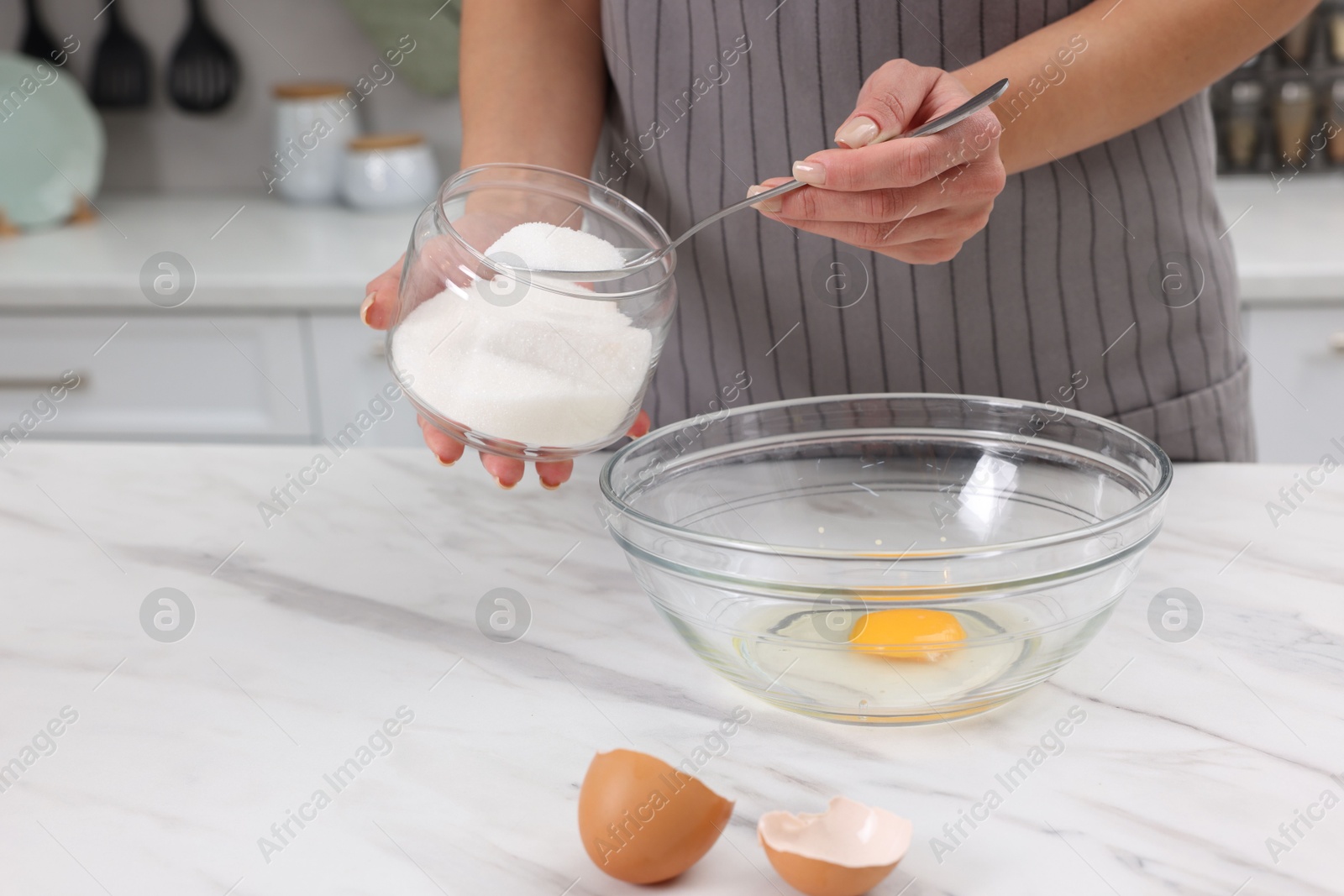 Photo of Making dough. Woman adding sugar into bowl with egg at white marble table, closeup