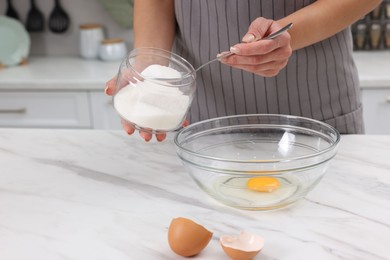 Photo of Making dough. Woman adding sugar into bowl with egg at white marble table, closeup