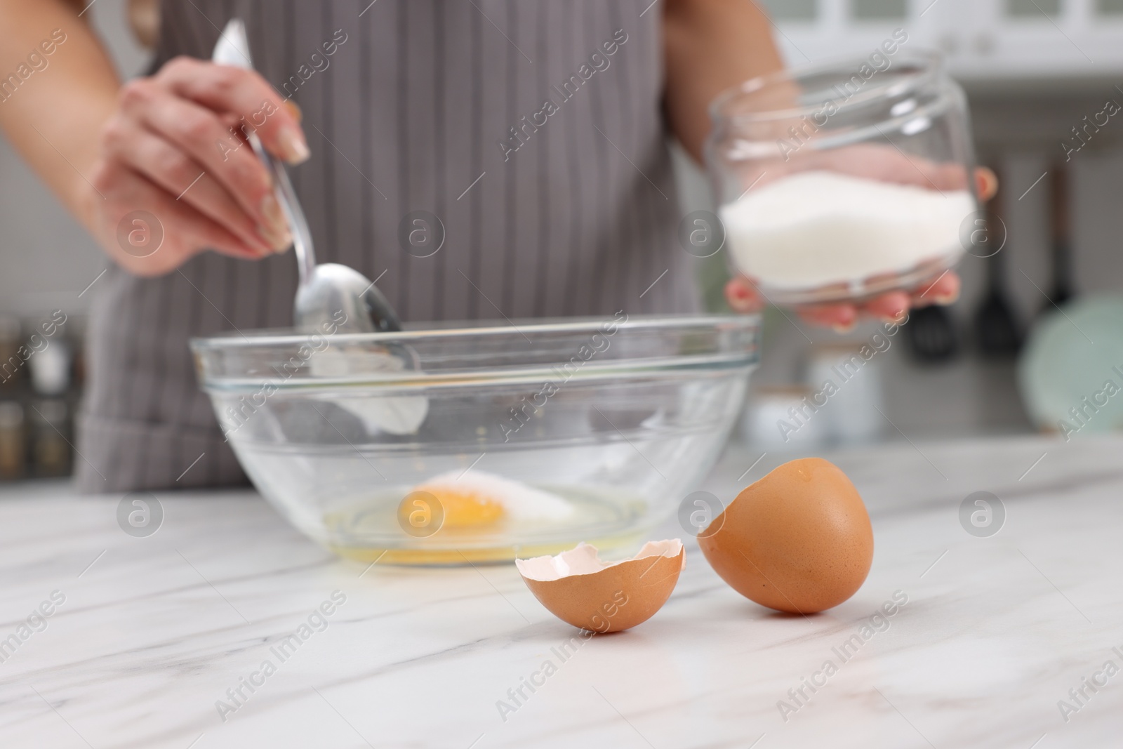 Photo of Making dough. Woman adding sugar into bowl with egg at white marble table, closeup