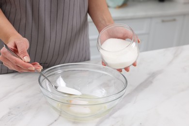 Photo of Making dough. Woman adding sugar into bowl with egg at white marble table, closeup