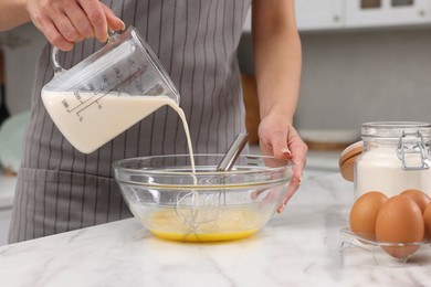 Photo of Making dough. Woman adding milk into bowl at white marble table, closeup