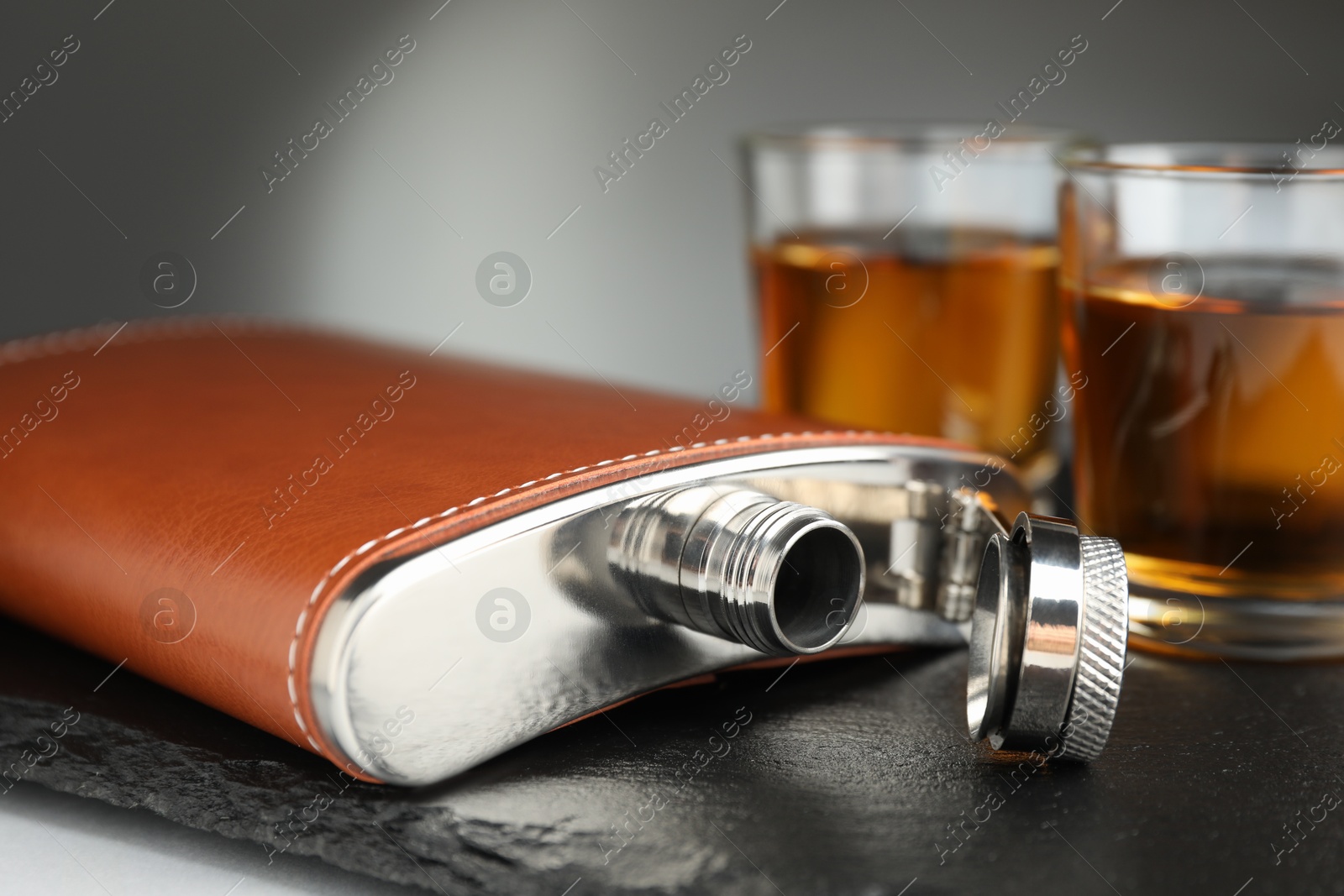 Photo of Hip flask and glasses of whiskey on table, selective focus