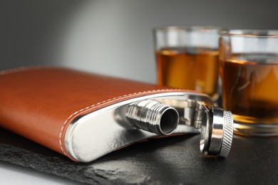 Photo of Hip flask and glasses of whiskey on table, selective focus