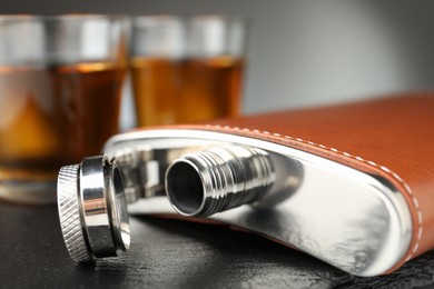 Photo of Hip flask and glasses of whiskey on table, selective focus