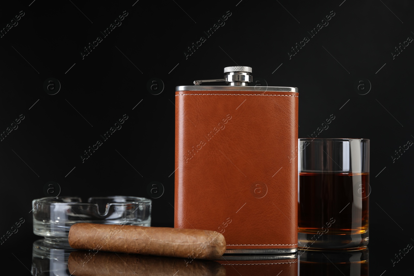 Photo of Hip flask, glass of whiskey, cigar and ashtray on black mirror surface