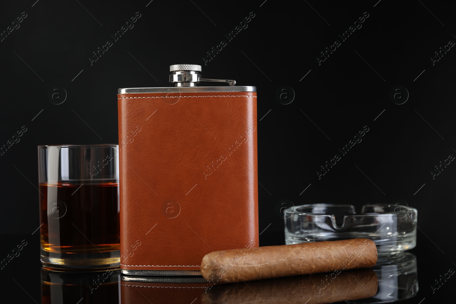 Photo of Hip flask, glass of whiskey, cigar and ashtray on black mirror surface