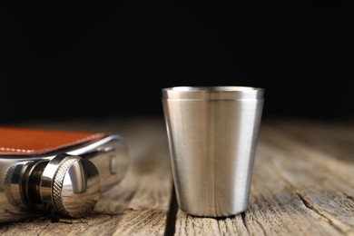 Photo of Hip flask and cups on wooden table, closeup