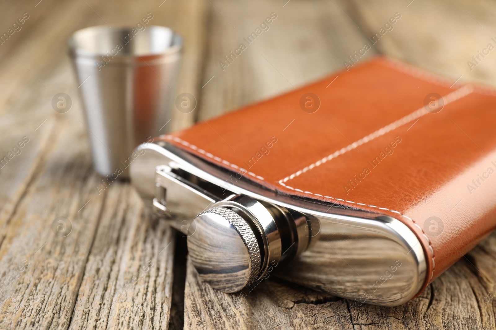 Photo of Hip flask and cups on wooden table, closeup