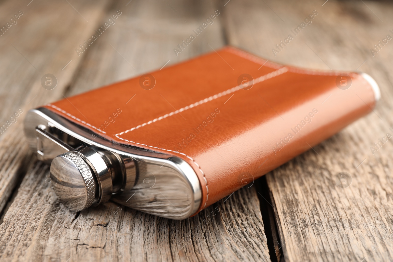 Photo of Leather hip flask on wooden table, closeup