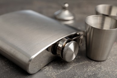 Photo of Hip flask, cups and funnel on grey table, closeup