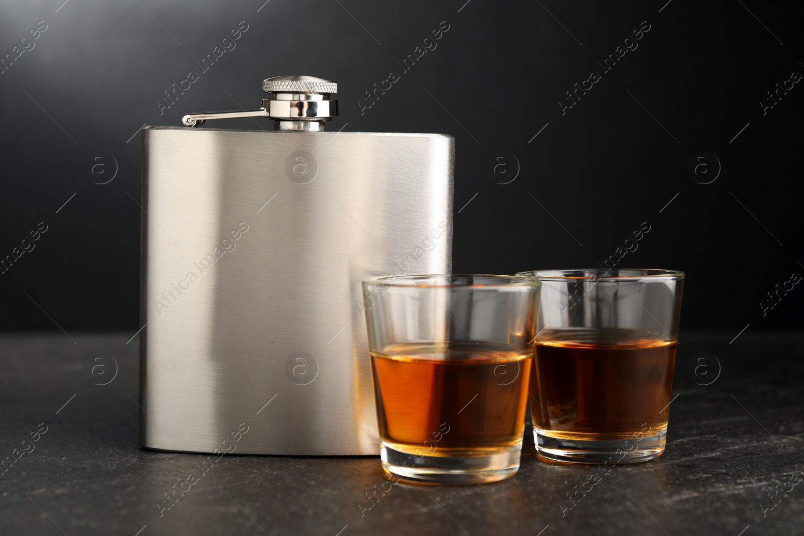 Photo of Hip flask and shot glasses of whiskey on black table