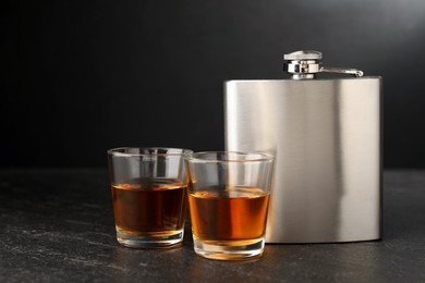 Photo of Hip flask and shot glasses of whiskey on black table