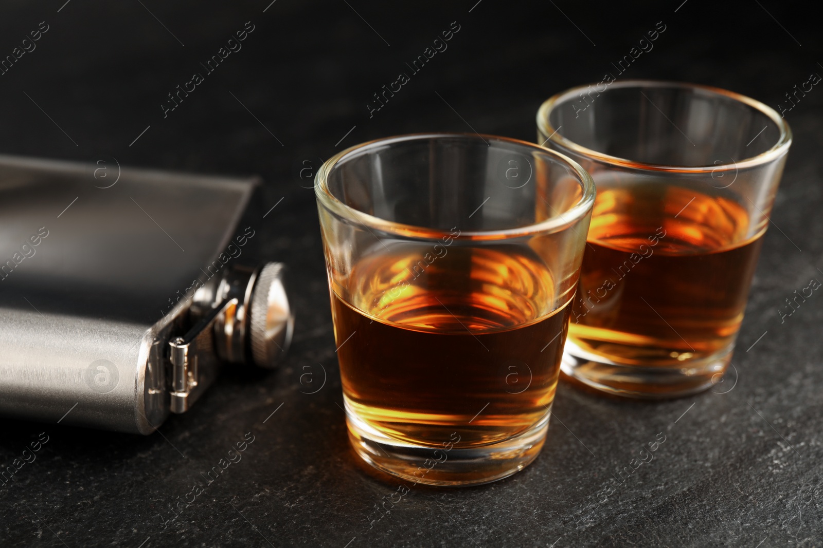 Photo of Hip flask and shot glasses of whiskey on black table, closeup