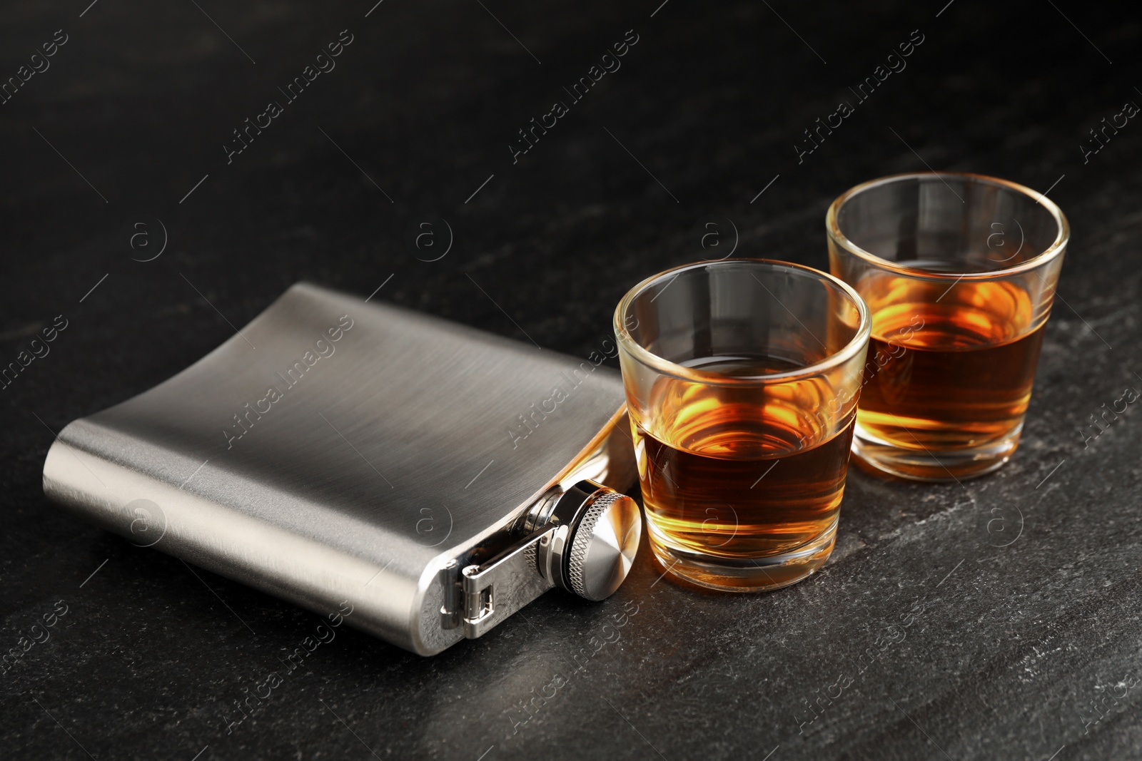 Photo of Hip flask and shot glasses of whiskey on black table, closeup