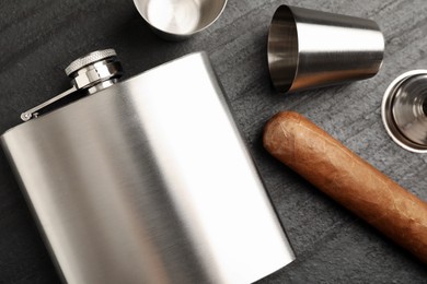 Photo of Hip flask, cups, funnel and cigar on black table, flat lay