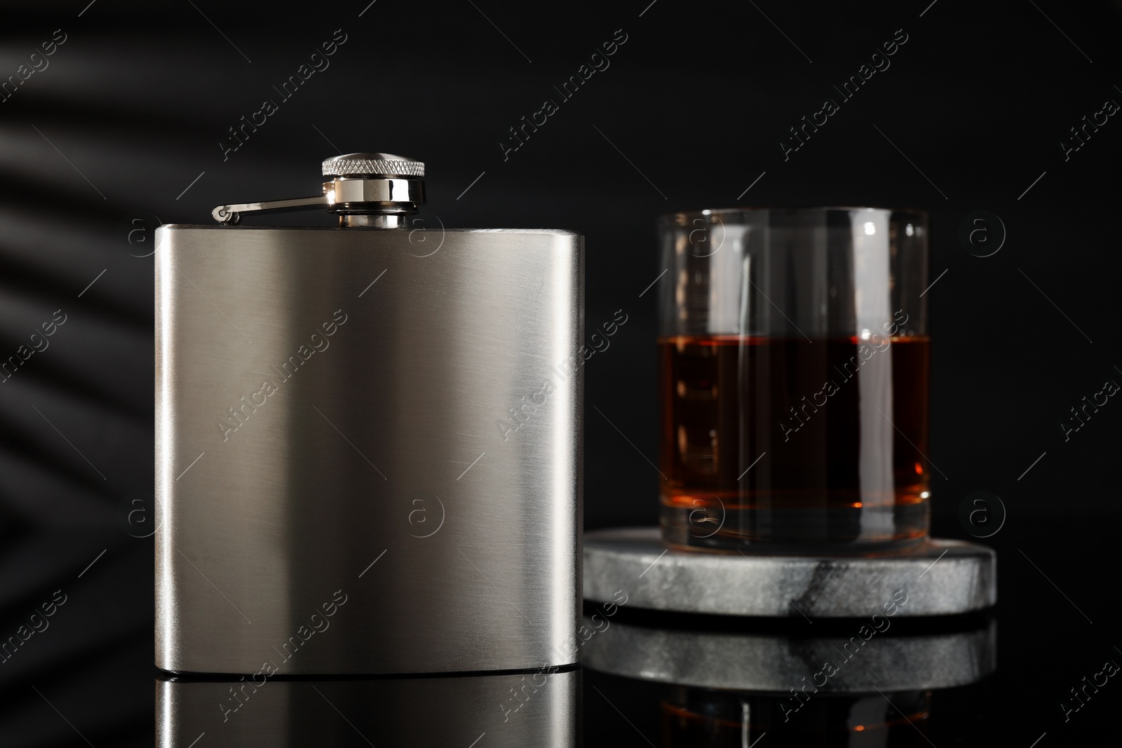 Photo of Hip flask and glass of whiskey on black mirror surface, closeup