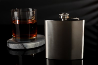 Photo of Hip flask and glass of whiskey on black mirror surface, closeup