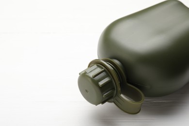 Photo of Green plastic canteen on white wooden table, closeup. Space for text