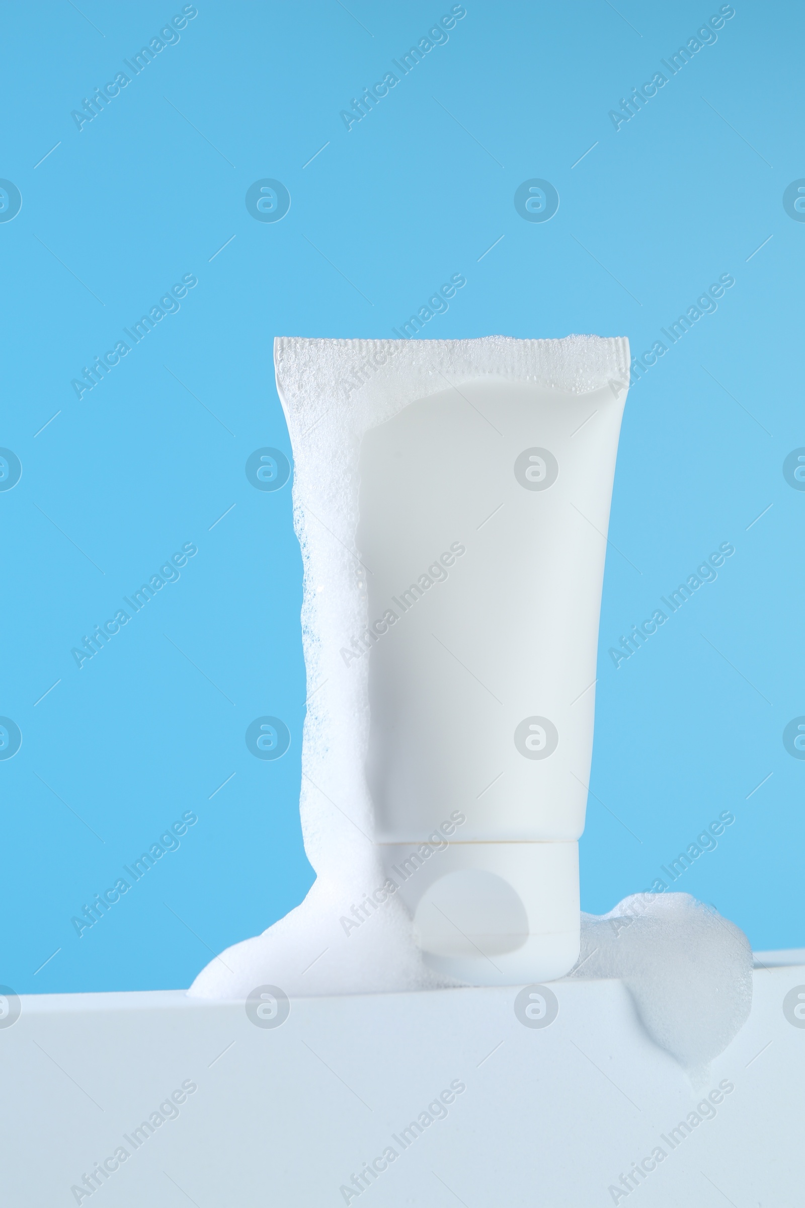 Photo of Tube of cosmetic product with foam on podium against light blue background