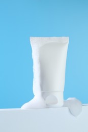 Tube of cosmetic product with foam on podium against light blue background