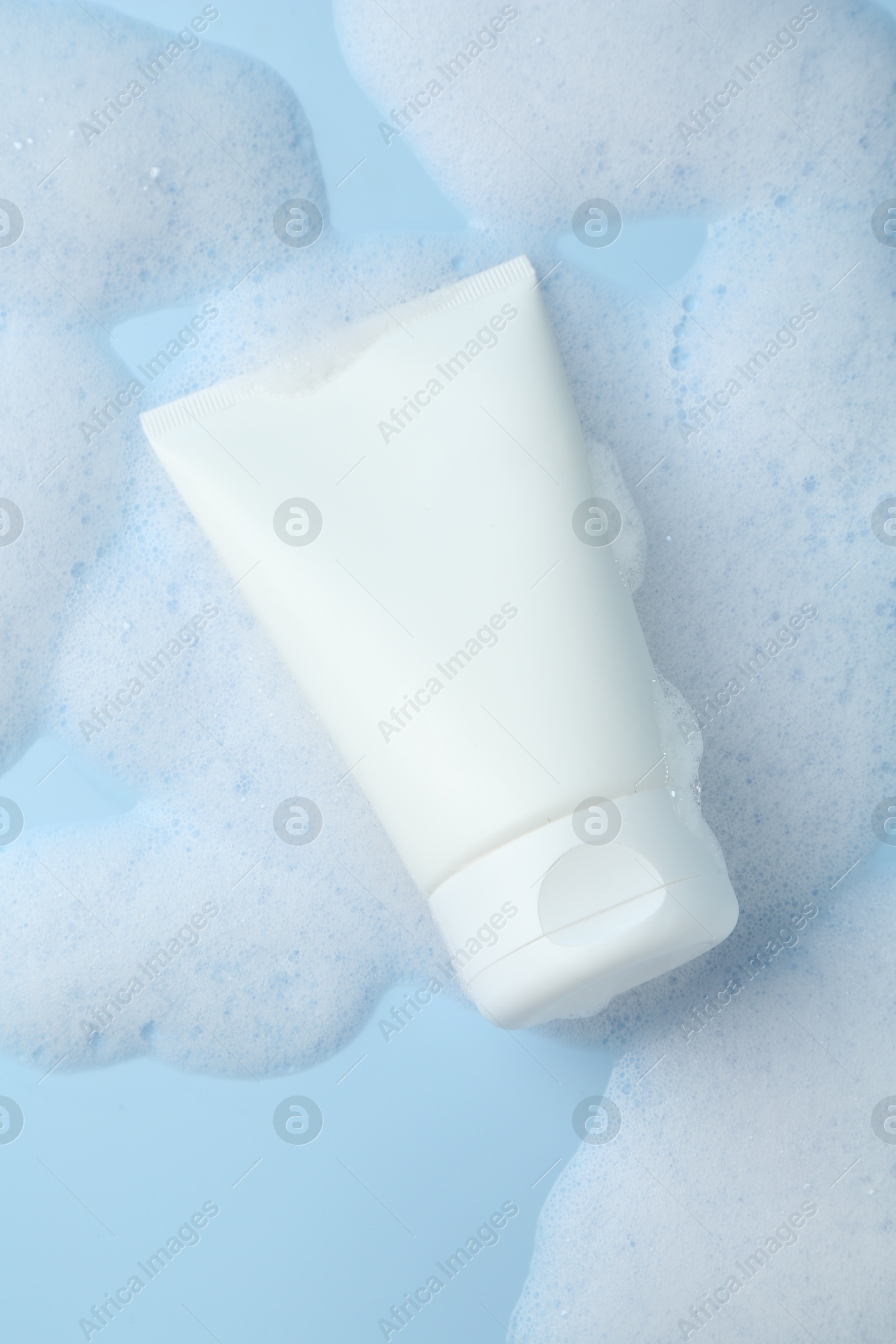 Photo of Tube of cosmetic product with foam on light blue background, top view