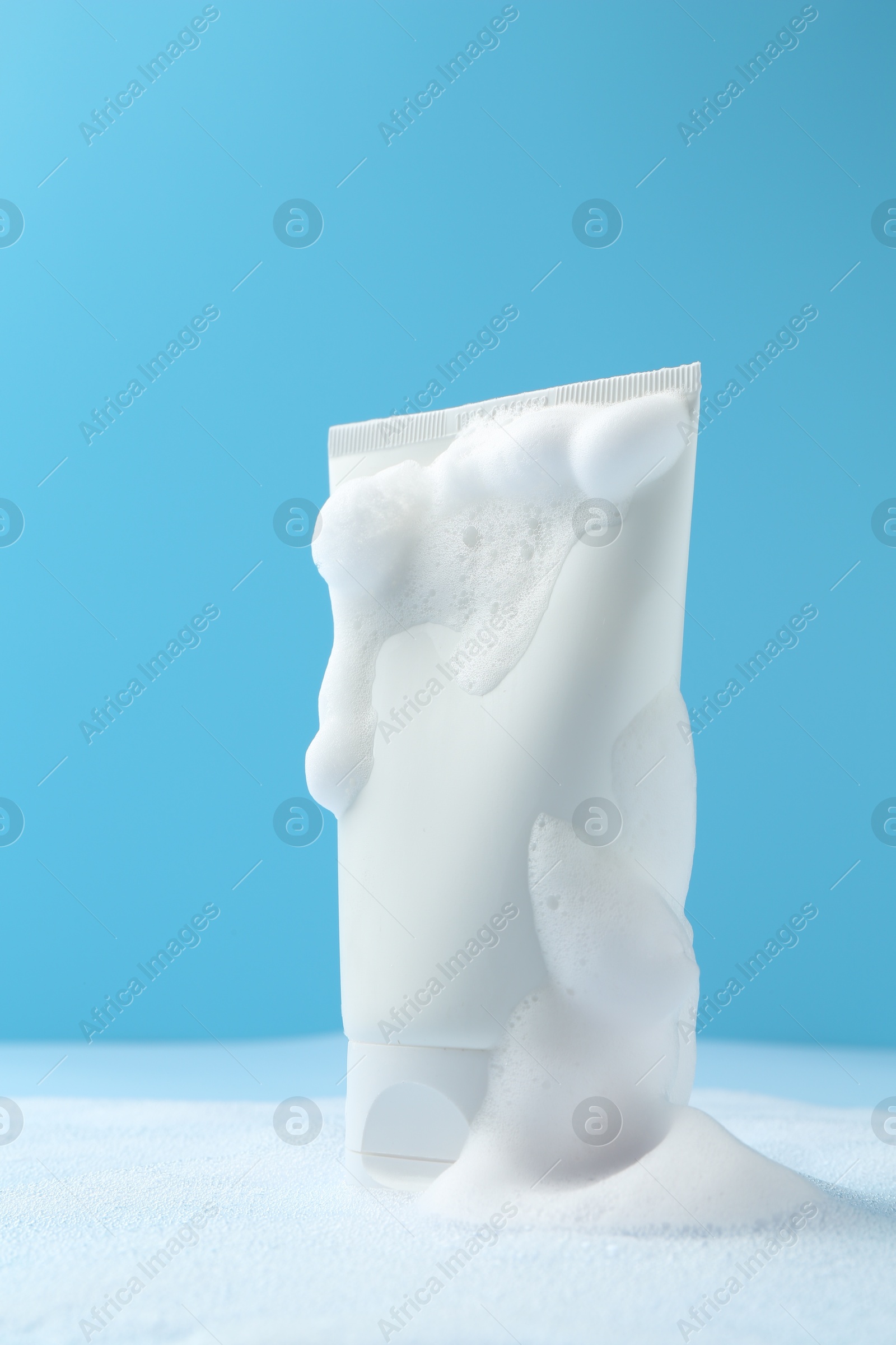 Photo of Tube of cosmetic product with foam on light blue background