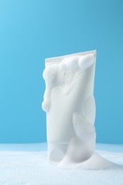 Photo of Tube of cosmetic product with foam on light blue background