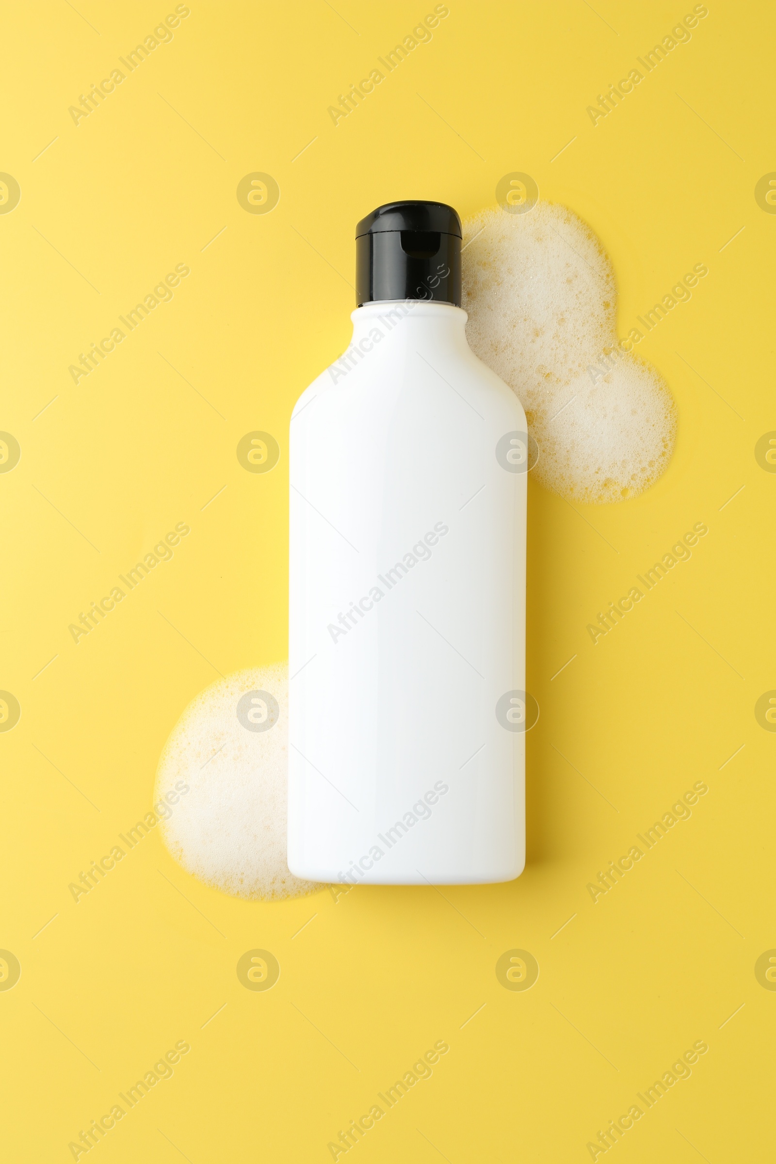 Photo of Bottle of cosmetic product with foam on yellow background, top view