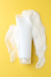 Photo of Tube of cosmetic product with foam on yellow background, top view