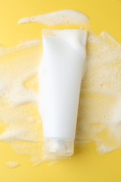 Photo of Tube of cosmetic product with foam on yellow background, top view