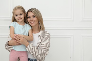 Happy mother and her cute little daughter near white wall indoors