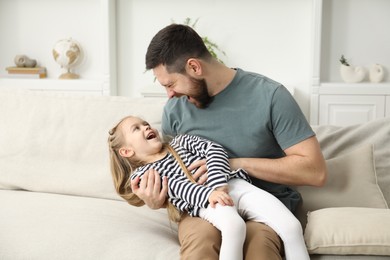 Happy father and his cute little daughter on sofa at home