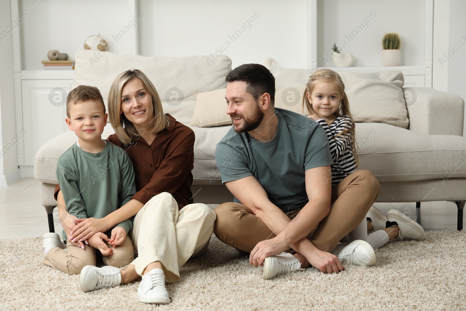 Photo of Happy parents and their children on rug at home