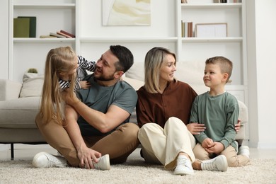 Happy parents and their children on rug at home