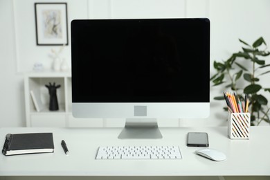 Photo of Modern workplace with computer and stationery on white desk indoors