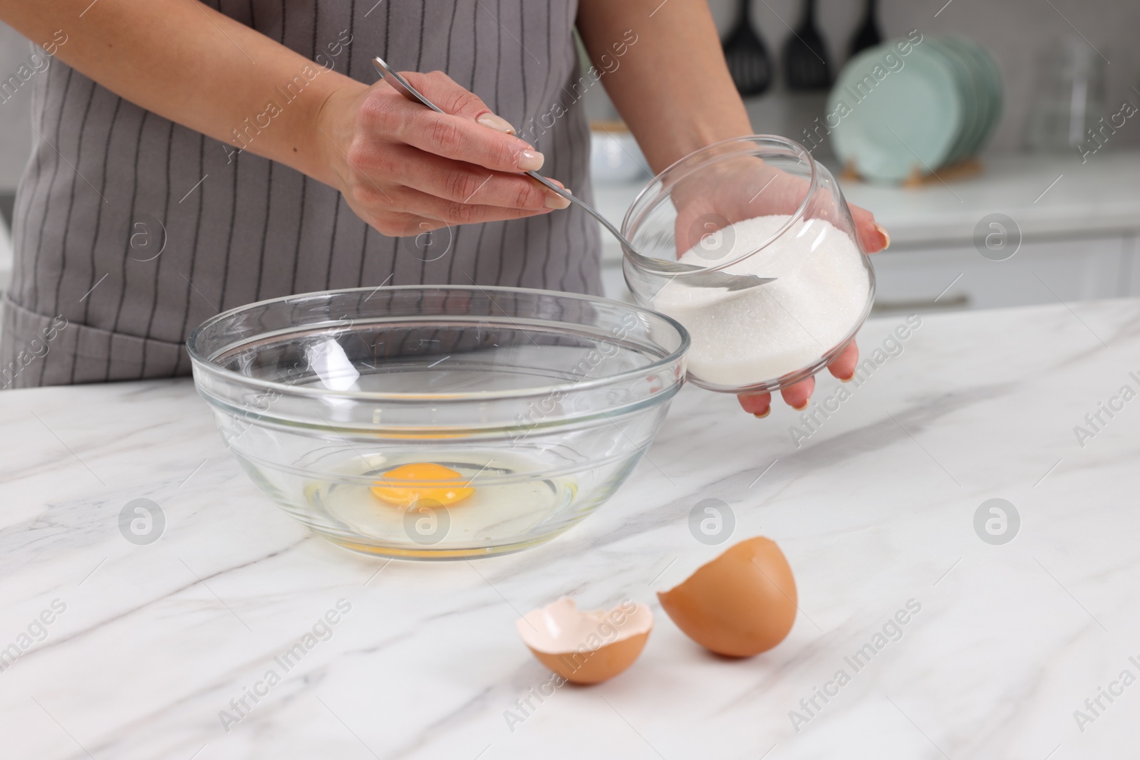 Photo of Making dough. Woman adding sugar into bowl with egg at white marble table, closeup