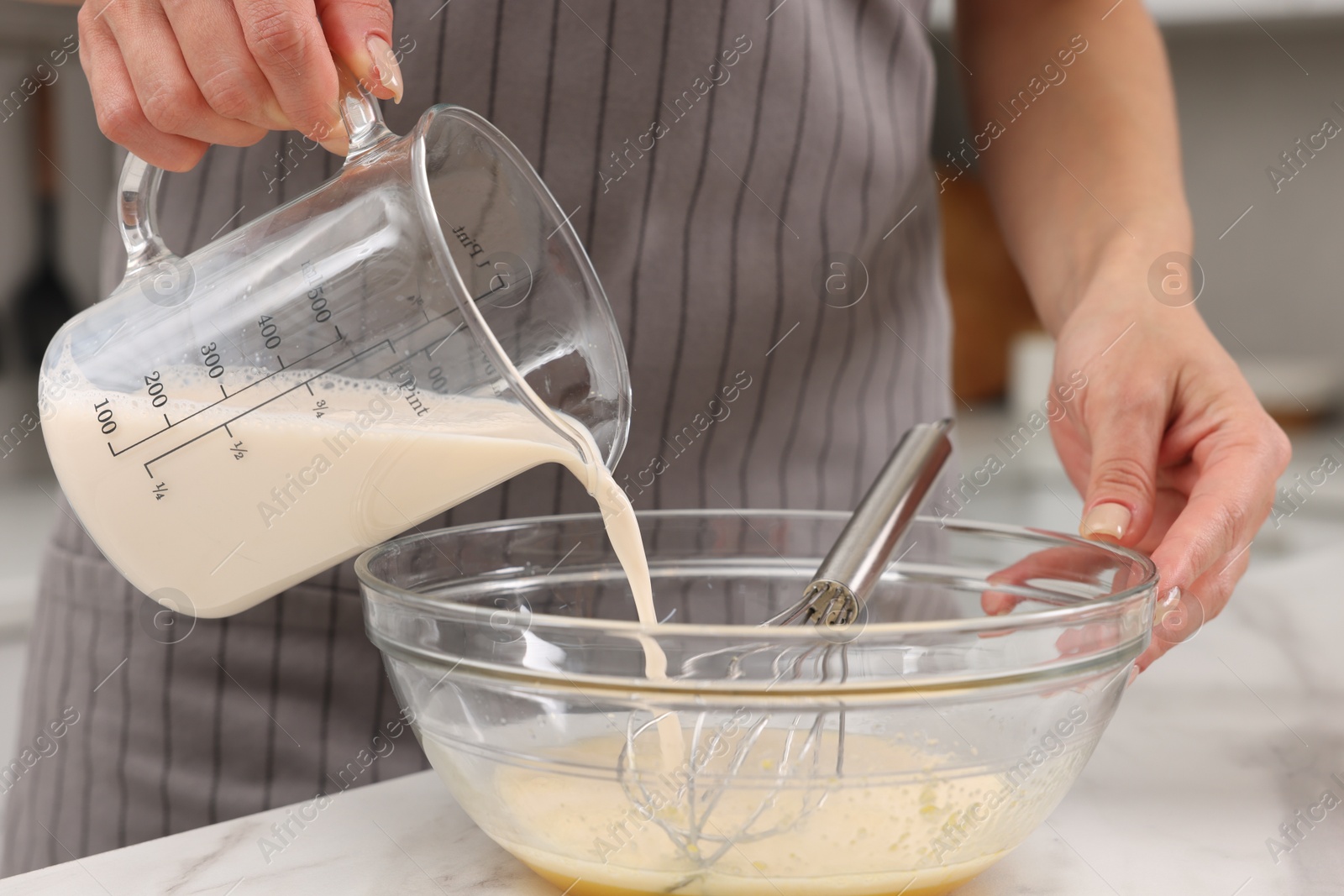 Photo of Making dough. Woman adding milk into bowl at white marble table, closeup