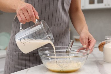 Photo of Making dough. Woman adding milk into bowl at white marble table, closeup