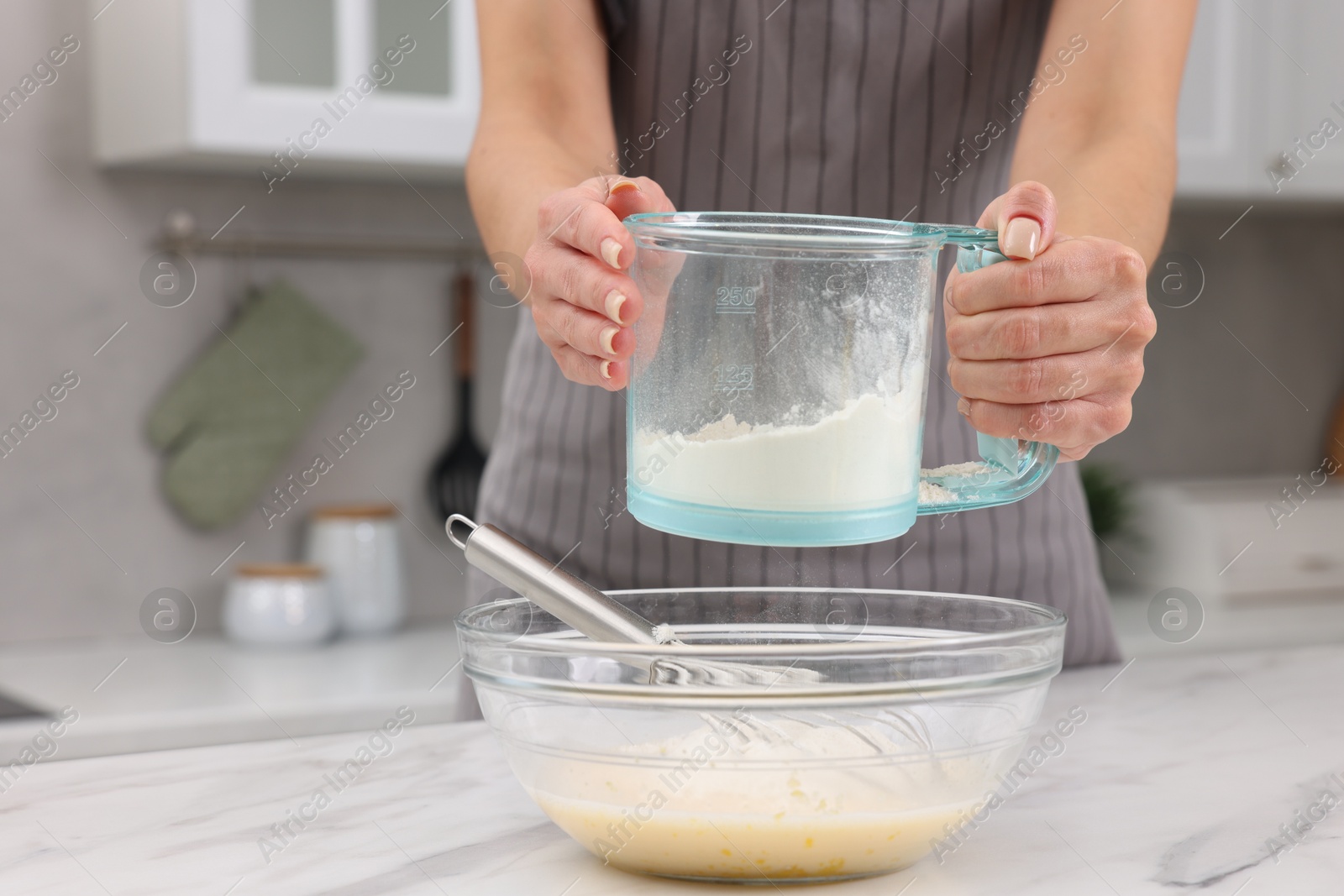 Photo of Woman adding flour into bowl with dough at white marble table, closeup