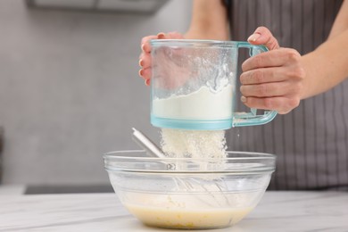 Photo of Woman adding flour into bowl with dough at white marble table, closeup