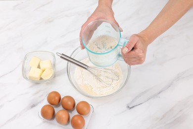 Photo of Woman adding flour into bowl with dough at white marble table, closeup