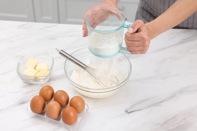 Woman adding flour into bowl with dough at white marble table, closeup