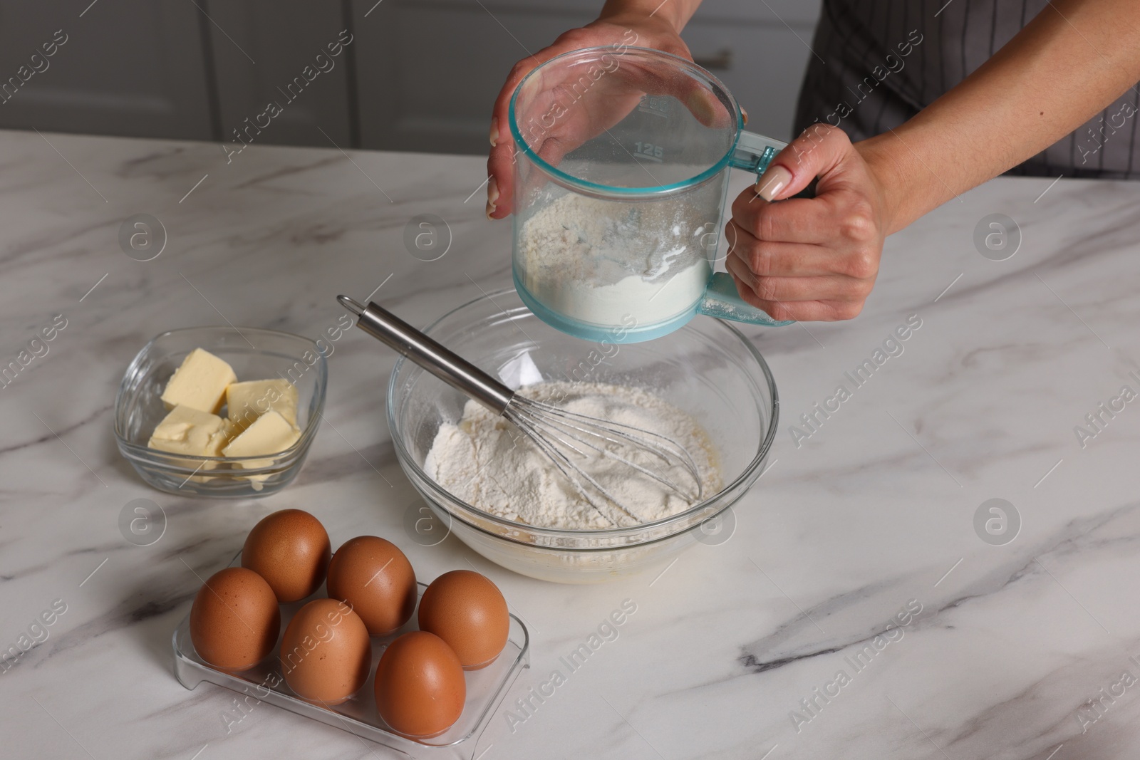 Photo of Woman adding flour into bowl with dough at white marble table, closeup