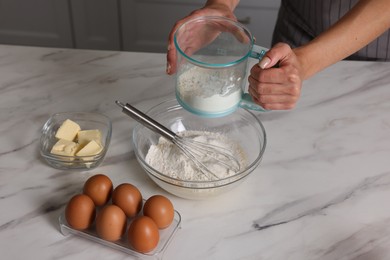 Photo of Woman adding flour into bowl with dough at white marble table, closeup