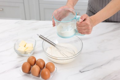 Photo of Woman adding flour into bowl with dough at white marble table, closeup