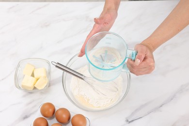 Photo of Woman adding flour into bowl with dough at white marble table, above view