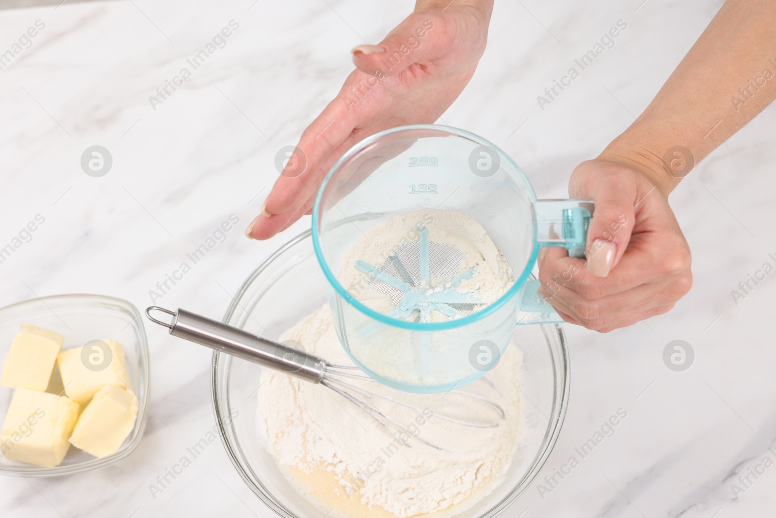 Photo of Woman adding flour into bowl with dough at white marble table, above view