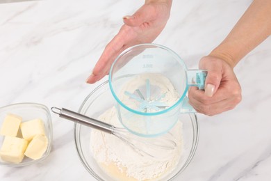 Photo of Woman adding flour into bowl with dough at white marble table, above view