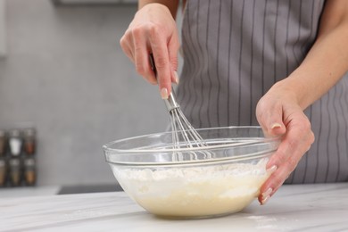 Photo of Woman making dough at white marble table indoors, closeup