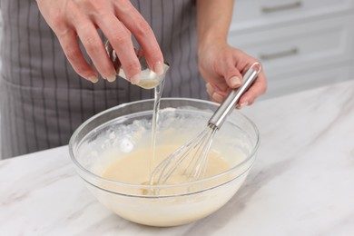 Woman adding oil into bowl with dough at white marble table, closeup